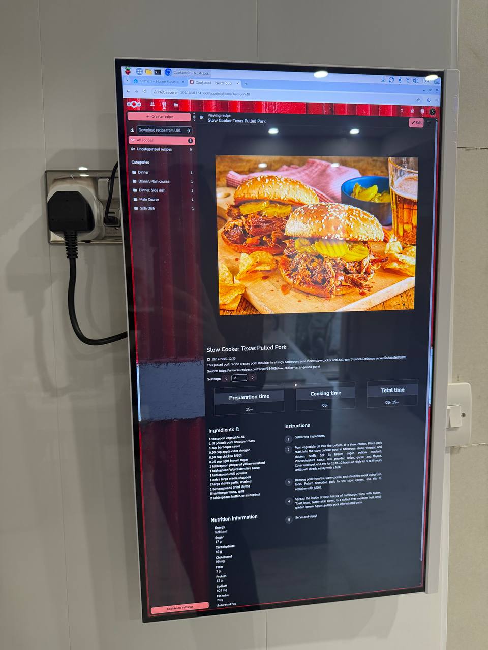 Wall-mounted smart kitchen display showing Nextcloud Cookbook recipe on a 27-inch touchscreen monitor, mounted in kitchen with Zigbee smart plug