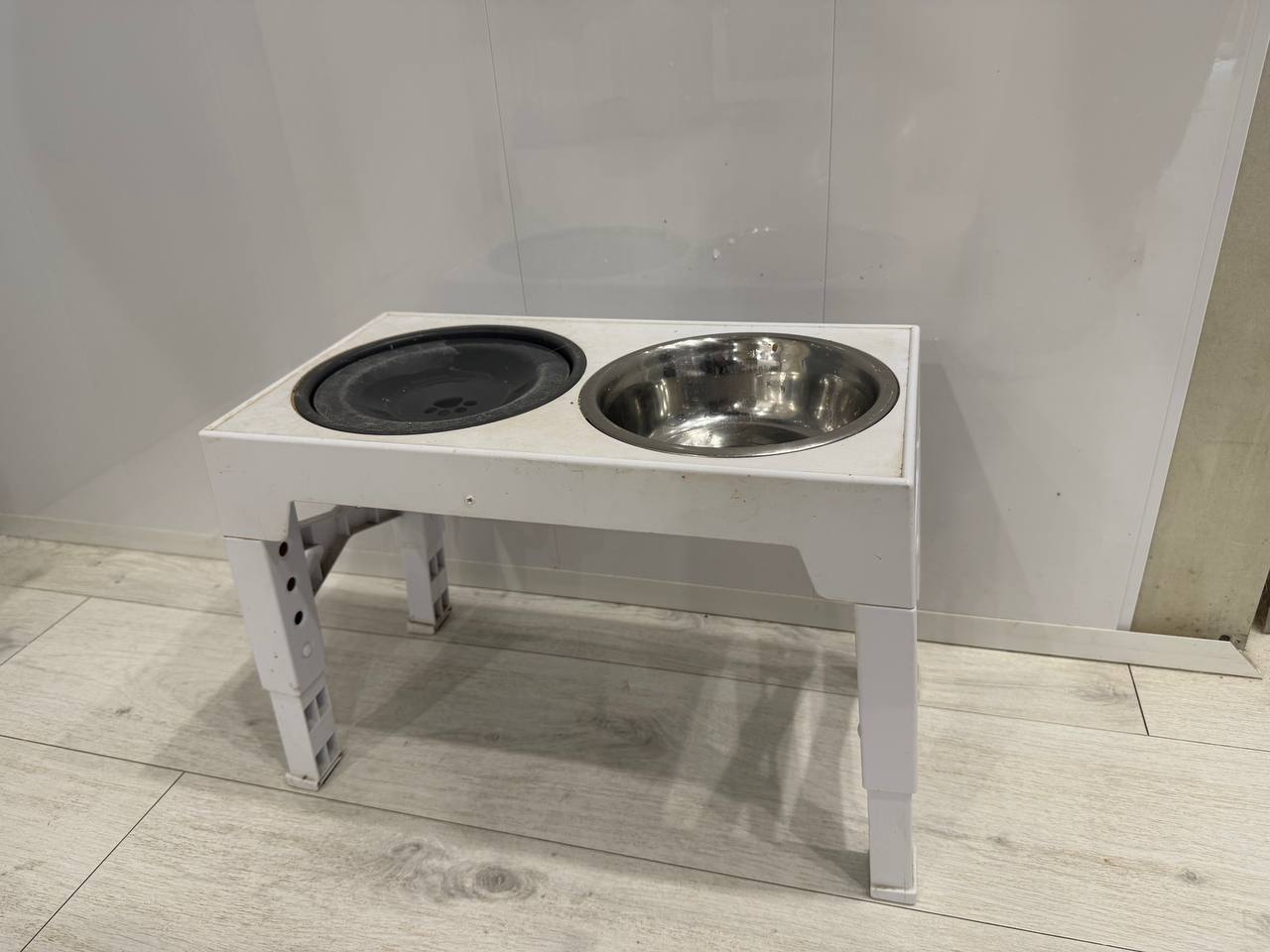 Polegas raised dog bowl stand at maximum height with one slow feeder bowl and one stainless steel water bowl, on light wood floor against white wall