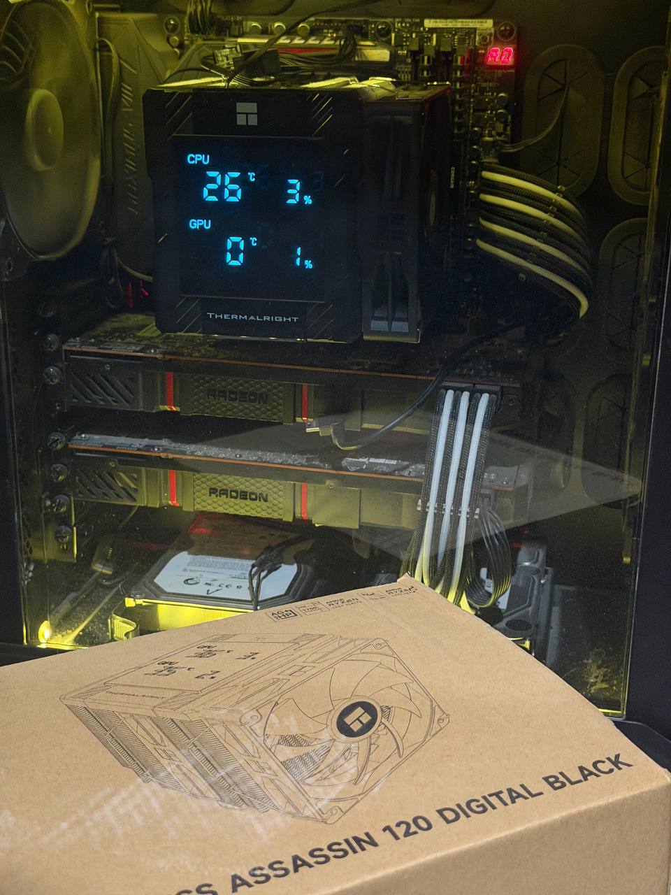 Thermalright Peerless Assassin 120 Digital Black installed in PC, digital display showing CPU 26°C at 3% load, dual AMD Radeon GPUs visible, box in foreground