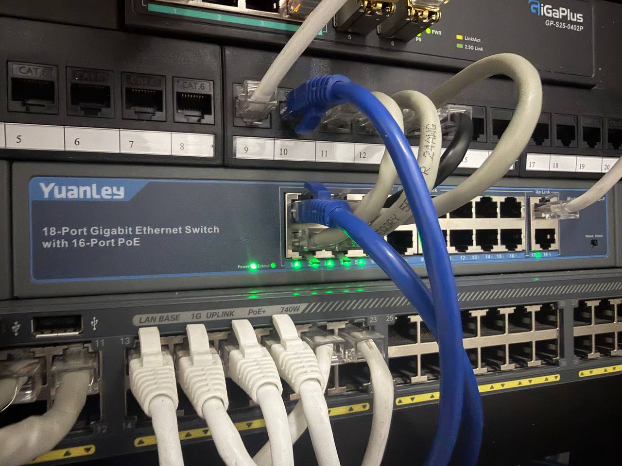 YuanLey 18-port Gigabit PoE switch installed in server rack with 5 Reolink PoE cameras connected via white Cat6 cables, green link lights active